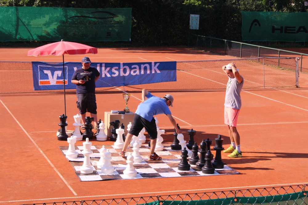 A few people play chess on a tennis court.